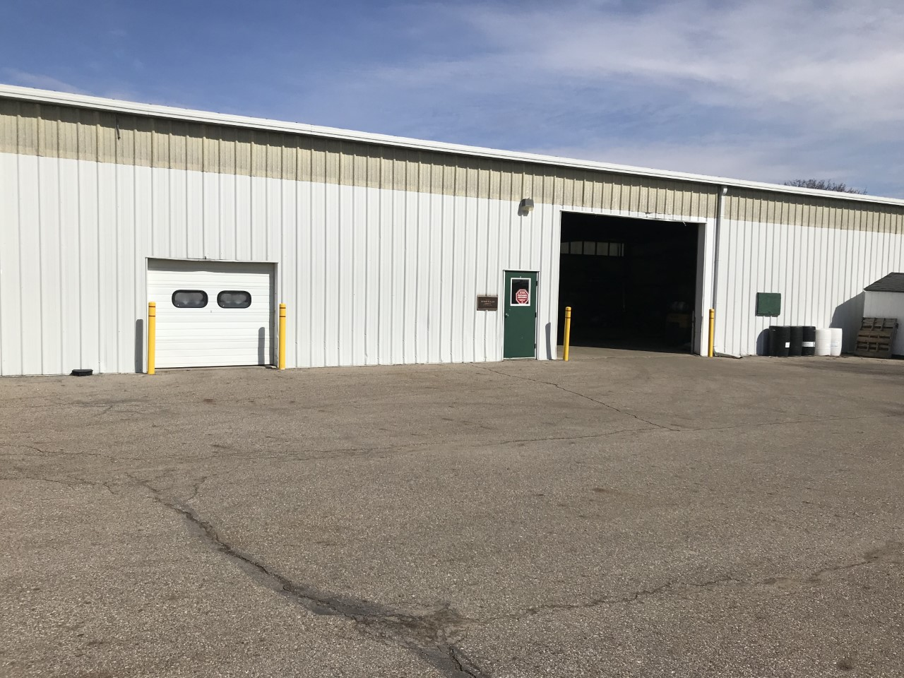 Image of white barn with small garage door on left man door then large open garage door on right. 